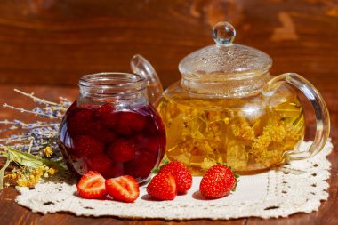 Taze çilek ve çaydanlık ıhlamur lavanta çayı ve ahşap arka plan üzerinde çiçekler ile kavanozda Çilek reçeli. Çilek ile taze ev yapımı çilek reçeli. Lezzetli çilek confiture ile Cam kavanoz