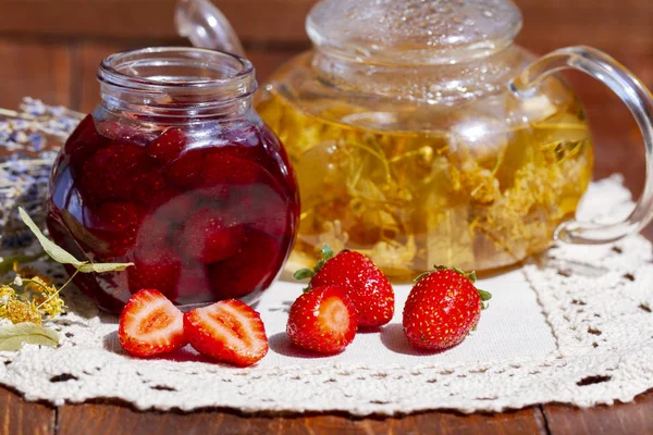 Tetera de tilo de lavanda té, flores y mermelada de fresa en frasco con fresas frescas en la mesa de madera. confitura de fresa de primer plano. mermelada de fresa casera con bayas por concepto natural orgánico . — Foto de Stock