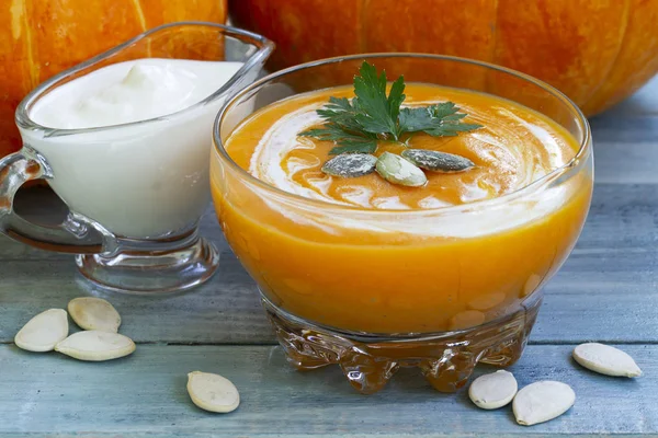 Roasted pumpkin and carrot soup with cream and pumpkin seeds on blue wooden background. Vegetarian autumn cream soup, tadka with cream and parsley. cream soup of pumpkin. Vegetarian autumn cream soup.