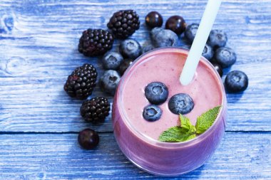 mavi ahşap arka plan üzerinde yaban mersini ve böğürtlen yüzlü. taze yaban mersini ve böğürtlen ile milkshake . malzemelerle meyve yüzlü. iyi olmak ve kilo kaybı kavramı. üst görünüm
