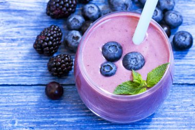 mavi ahşap arka plan üzerinde yaban mersini ve böğürtlen yüzlü. taze yaban mersini ve böğürtlen ile milkshake . malzemelerle meyve yüzlü. iyi olmak ve kilo kaybı kavramı. üst görünüm