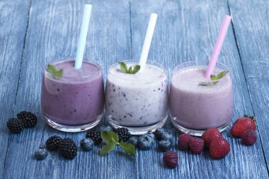 Ahududu, çilek, böğürtlen, mavi ahşap arka plan üzerinde yaban mersini yüzlü. taze çilek ile milkshake. malzemelerle sağlıklı meyve yüzlü. iyi olmak ve kilo loos kavramı