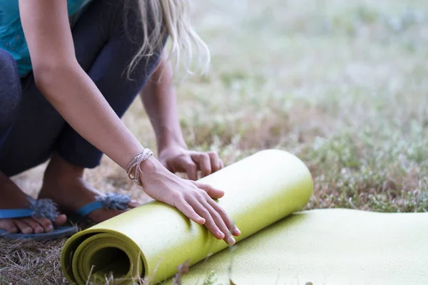 Abgeschnittenes Bild von Mädchen, die Yogamatte rollen. Nahaufnahme einer attraktiven jungen Frau, die grüne Yoga- oder Fitnessmatten faltet, nachdem sie auf einer Lichtung im Wald oder im Stadtpark trainiert hat. Gesundes Leben — Stockfoto