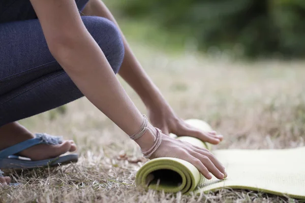 Abgeschnittenes Bild von Mädchen, die Yogamatte rollen. Nahaufnahme einer attraktiven jungen Frau, die grüne Yoga- oder Fitnessmatten faltet, nachdem sie auf einer Lichtung im Wald oder im Stadtpark trainiert hat. Gesundes Leben — Stockfoto