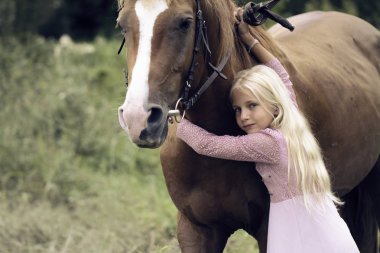 ormanda at ile masum sarışın kız. pembe bir elbise uzun sarışın saçlı güzel beyaz kız kahverengi bir at yatıyor ve onu sarılıyor. masum çocukluk kavramı. at üstüne yalınayak çocuk.