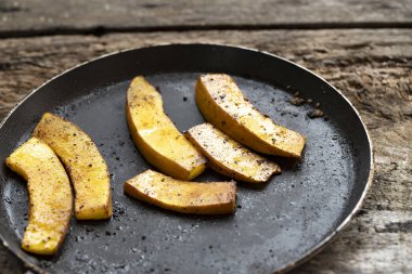Tavada kızartılmış baharatlı balkabağı, ahşap bir kırsal masada. Geleneksel sonbahar yemekleri. Vejetaryen yemeği. Yemek pişiriyorum. Aile yemeği. Şükran Günü konsepti. Sonbahar kompozisyonu. Yaşam tarzı, özgün