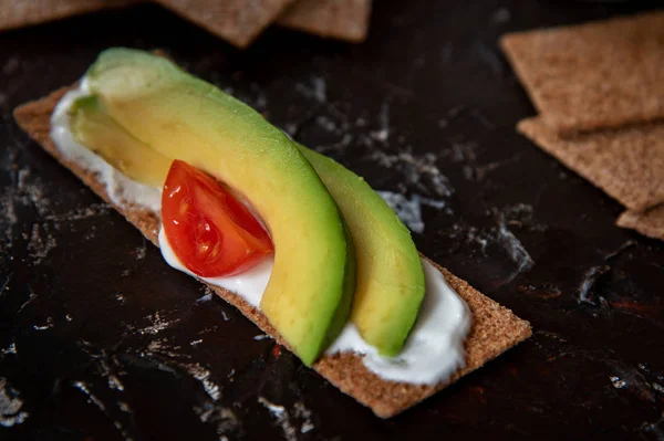 Snack saludable de galleta de pan crujiente de centeno integral con tomates Cherry, aguacate y yogur sobre fondo negro — Foto de Stock