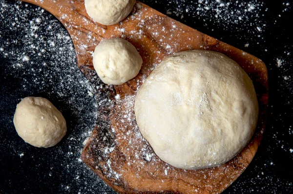 Deeg voor brood of pizza op een bord. Zwarte achtergrond — Stockfoto