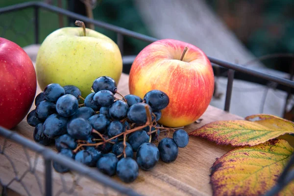 Cosecha de otoño. Manzana, uvas y hojas amarillas en la bandeja de madera, al aire libre — Foto de Stock