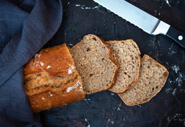 Taze pişmiş ev yapımı ekşi ekmek, siyah arka planda dilimlenmiş..