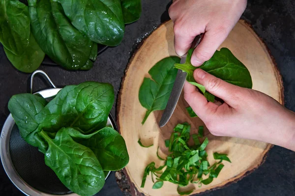 A woman is cutting fresh spinach on a cutting board.