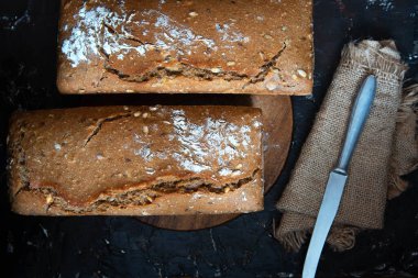 Ev yapımı taze pişmiş tam tahıllı çavdar ekmeği ve siyah arka planda tohumlar..