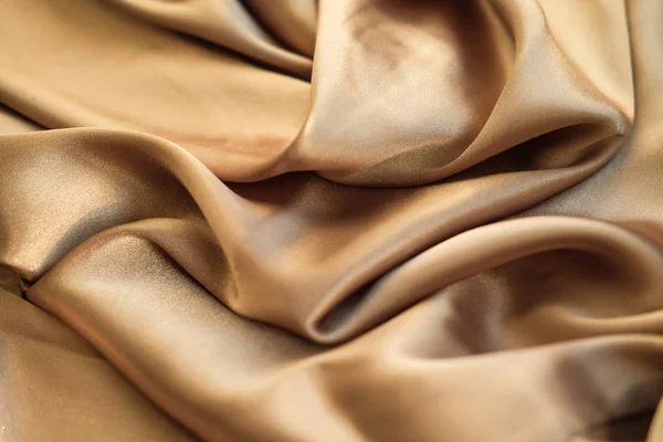 The gold fabric is laid out waves. Satin fabric. Brown material — Stock Photo, Image