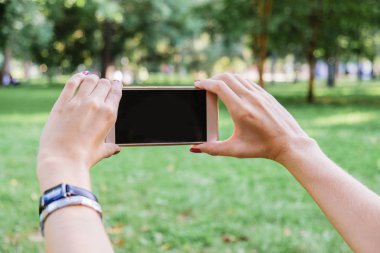 Kadın yeşil park Caddesi üzerinde dokunmatik ekran akıllı telefon kısa mesaj veya reklam içeriği için boş kopya alanı ekranlı holding.