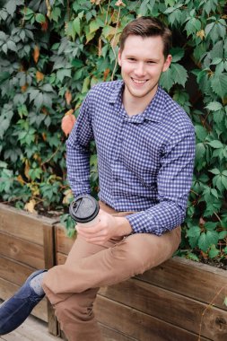 Gülümseyen adam ekose gömlek ve pantolon bir smartphone kullanarak. At break kahve içme başarılı genç işadamı. 