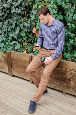 Gülümseyen adam ekose gömlek ve pantolon bir smartphone kullanarak. At break kahve içme başarılı genç işadamı. 