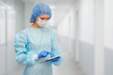 Koruyucu giysili kadın doktor: tıbbi maske, şapka ve bornoz. Kadın dijital tablet kullanıyor ve ekranda hastalık istatistikleri gösteriyor..