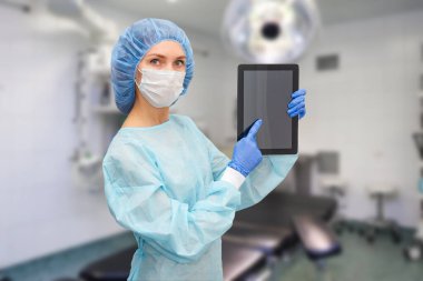 Koruyucu giysili kadın doktor: tıbbi maske, şapka ve bornoz. Kadın dijital tablet kullanıyor ve ekranda hastalık istatistikleri gösteriyor..