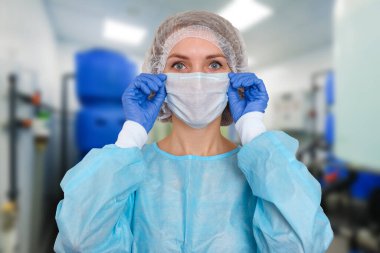 Önlüklü doktor portresi. Korunaklı şapkalı ve yüz maskeli bir kadın doktor. Koronavirüse karşı güvenlik önlemleri almış..