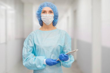 Koruyucu giysili kadın doktor: tıbbi maske, şapka ve bornoz. Kadın dijital tablet kullanıyor ve ekranda hastalık istatistikleri gösteriyor..