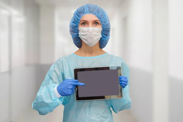 Female doctor in protective suit: medical mask, hat and robe. The woman uses a digital tablet and displays disease statistics on the screen.
