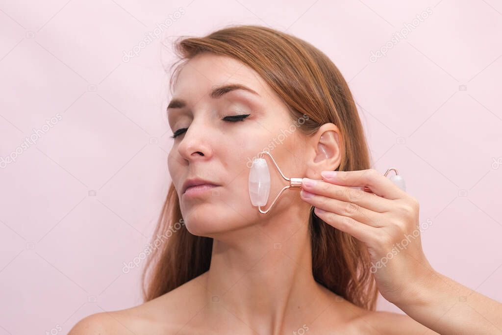 A young beautiful woman is doing a facial massage with a jade roller. Roller massager for smoothing wrinkles on the face.
