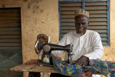 Yerel bir terzi, eski bir dikiş makinesinde renkli kumaşla çalışır. Gelenek ve işçiliği yansıtır..