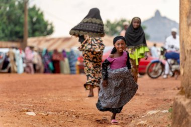 A young girl in traditional attire runs with a joyful smile, capturing the spirit of childhood and vibrant culture in Cameroon.