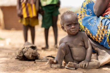 A young Mbororo child sits by the mother, reflecting innocence and the authentic everyday life of an African village.