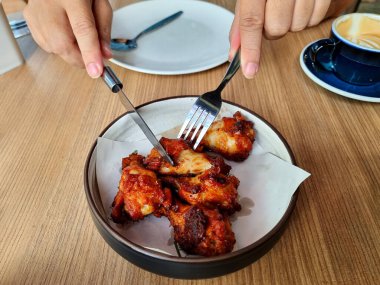 Kadınların elleri, ahşap bir masada kızarmış tavuk kanatlarını kesmek için çatal ve bıçak kullanırdı..