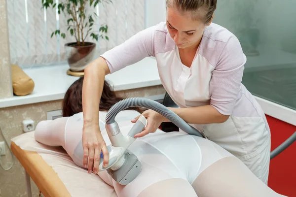 Woman having procedure of anti cellulite lpg treatment massage with therapist and apparatus in cosmetology clinic