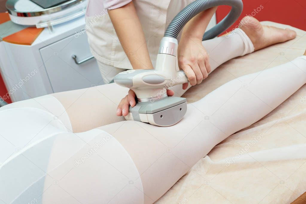 Woman having procedure of anti cellulite lpg treatment massage with therapist and apparatus in cosmetology clinic