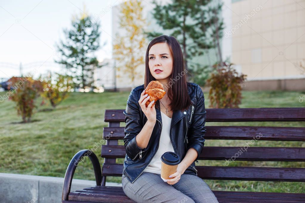 Handsome caucasian woman sitting in park and eating croissant with coffee