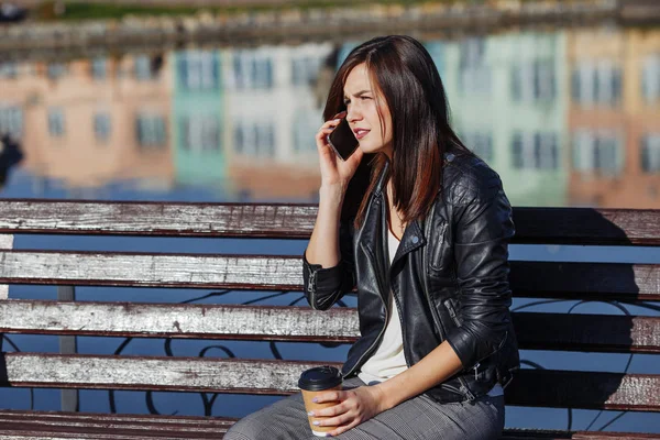 Handsome smiling caucasian woman with mobile phone sitting in park