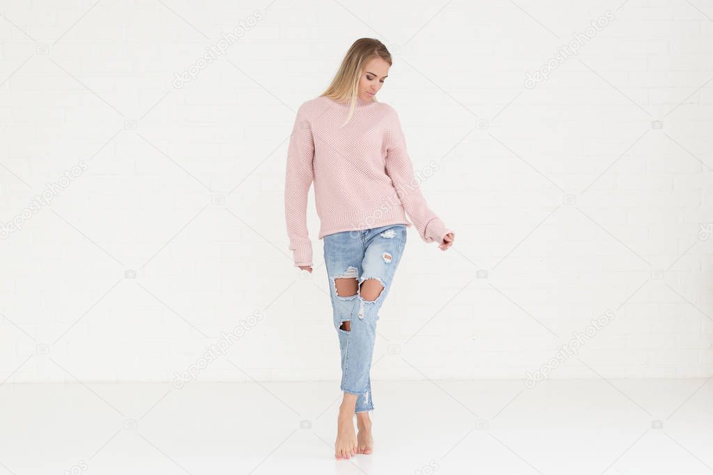 Fashion portrait of woman in pink casual sweater and ripped jeans