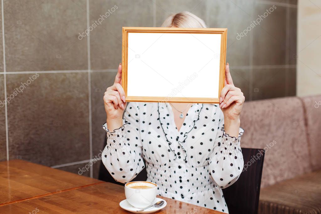 Business woman in cafe holding wooden frame, blank white mockup