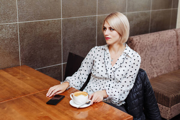 Woman sitting in cafe with coffee and smartphone
