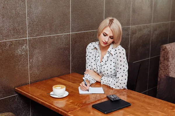 Business woman in cafe sitting and writing in notebook