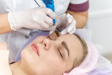 Kalıcı makyaj, kaş dövmesi. Beyaz eldivenli kozmetolog güzellik salonundaki kadının makyaj makinesiyle makyaj yapıyor.