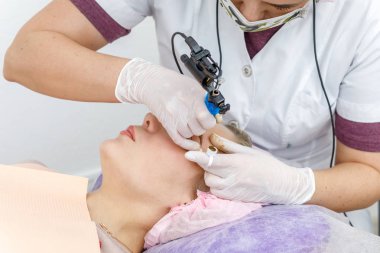 Kalıcı makyaj, kaş dövmesi. Beyaz eldivenli kozmetolog güzellik salonundaki kadının makyaj makinesiyle makyaj yapıyor.