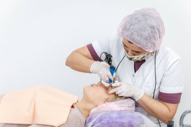 Kalıcı makyaj, kaş dövmesi. Beyaz eldivenli kozmetolog güzellik salonundaki kadının makyaj makinesiyle makyaj yapıyor.