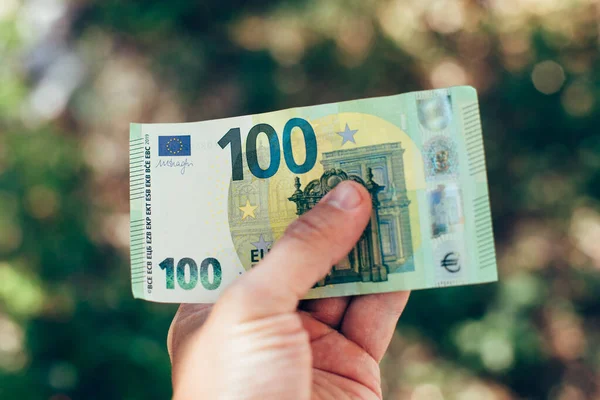 Male hand holding 100 hundredth euro banknote on green background — Stock Photo, Image