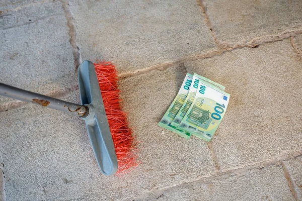Горничная метла подметает сотую банкноту евро на улице — стоковое фото
