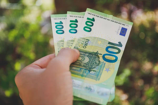 Мужская рука держит банкноты в 100 евро на зеленом фоне — стоковое фото