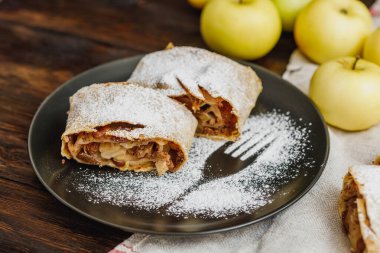 Kremalı elmalı turta ve siyah tabakta kuru üzüm, ahşap arka plan.