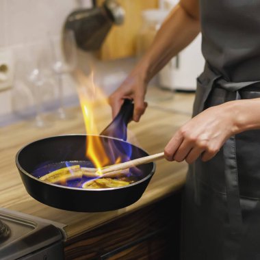 Woman preparing caramelized banana flambe with cognac in frying pan and sets fire clipart