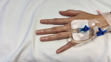 Tıbbi bir ortamda damar içi tedavi (IV damlası) gören bir kadının eli.