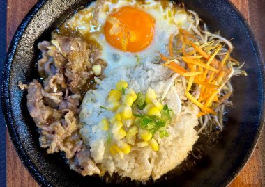 Mükemmel kızartılmış güneşte kızartılmış yumurta ve ızgara et ya da tatlı mısırlı biftek dilimleri, dilimlenmiş bahar soğanı ve havuç parçaları cızırdayan siyah ocakta yakın plan pırasa parçaları..