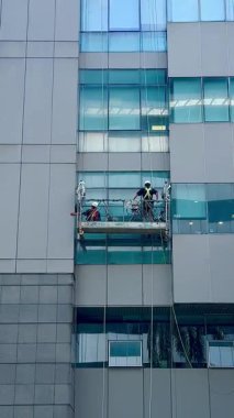 Gondoldaki profesyonel cam temizleme işçileri. İki işçi, önleyici bakım ve onarım tedbiri olarak gökdelenin pencerelerine erişmek ve onları temizlemek için özel ekipman kullanıyor.