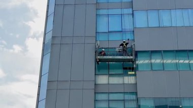 Gondoldaki profesyonel cam temizleme işçileri. İki işçi, önleyici bakım ve onarım tedbiri olarak gökdelenin pencerelerine erişmek ve onları temizlemek için özel ekipman kullanıyor.